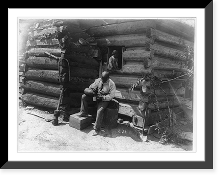 Historic Framed Print, [Afro-American man seated outside log cabin, pouring drink into cup and girl seated in window of the cabin],  17-7/8" x 21-7/8"