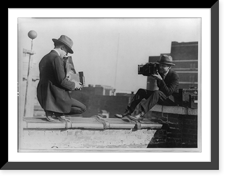Two photographers taking each others' picture with hand-held cameras while perched on roof, Historic Print
