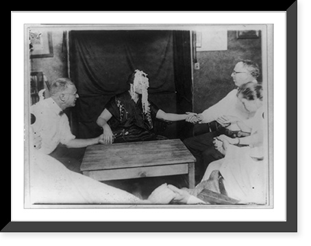 Woman medium with ectoplasm" all over her face, holding hands with two men and others at table during a seance(?)", Historic Print