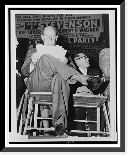 Adlai E. Stevenson, full-length portrait, seated, facing front, studying his speech notes, at a campaign rally in the Harlem section of New York City, Vintage Poster