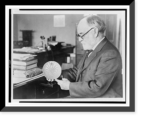 Dr. J. Walter Fewkes, seated at desk, facing left, examining disk showing figure entering maze, Vintage Poster