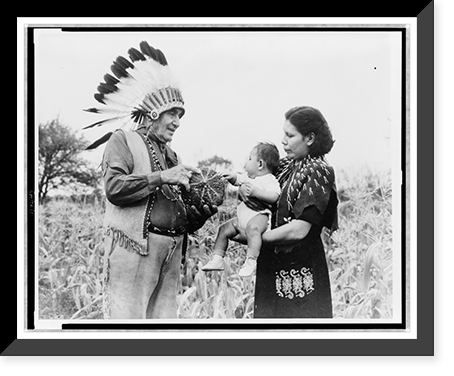 Mrs. Marion John Miles holding baby, while Oneida Chief William H. Rockwell demonstrates how stripes on squash determine the celebration of the gathering of the harvest, Oneida Lake, New York Cla