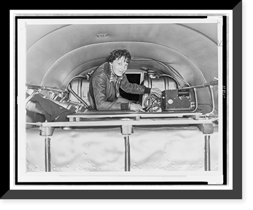 Historic Framed Print, [Amelia Earhart, seated in airplane, checking equipment],  17-7/8" x 21-7/8"