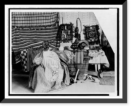 Man from Togo sitting in display of market goods, Historic Reproduction
