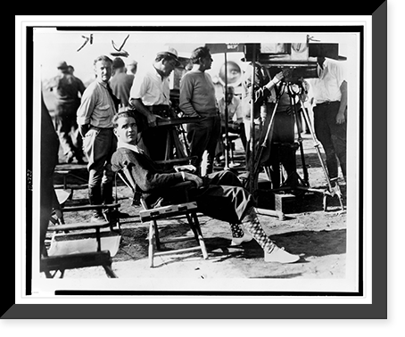 Howard Hughes, full-length portrait, seated, facing front, film crew in background, during filming of Sky devils"" Classic, Antique Print