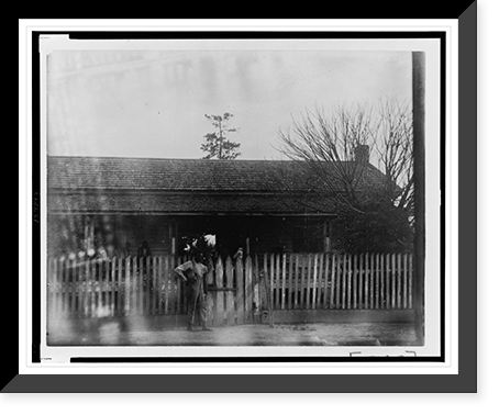 African American man standing at tall picket fence in front of house, Vintage Poster