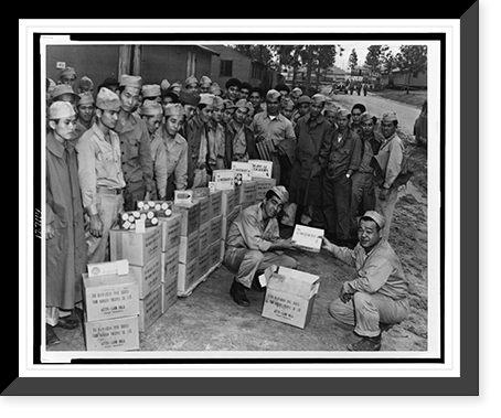 Private Sam Oka hands over to Private Henry Oshiro his share of the generous gifts of candies and cigarettes sent to members of the Japanese-American Combat Team by a Hawaiian pineapple company Her