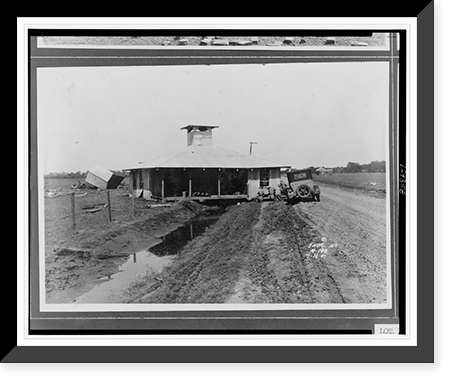 Building, moved by floodwaters, straddling drainage creek, to the right, car parked on gravel road, to the left, smaller building toppled onto its side.Ewing, Inc. Classic, Historic Print