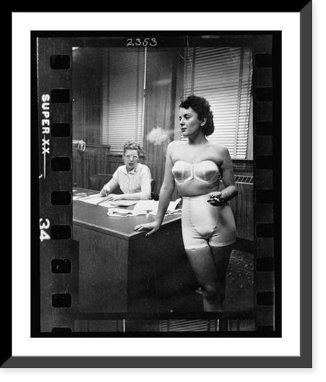 Historic Framed Print, [Woman model, standing in an office, smoking while modeling undergarments],  17-7/8" x 21-7/8"