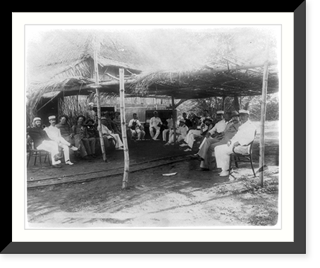 Group of American soldiers posed under thatched-roof outside, piano and man with violin, San Roque (Cavite), Philippines, Antique Print