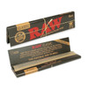 A detailed close-up image of a single pack of RAW® Black King Size Slim Rolling Papers. The focus is on the intricate watermark and the translucent, light brown color of the unbleached paper, showcasing its natural and less processed quality. The image also highlights the thinness of the papers, appealing to those who prefer a purer and more refined smoking experience. This visual representation emphasizes the artisan craftsmanship and eco-friendly attributes of the product