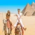 Travellers riding a camel in front of the Pyramids of Giza, Cairo, Egypt
