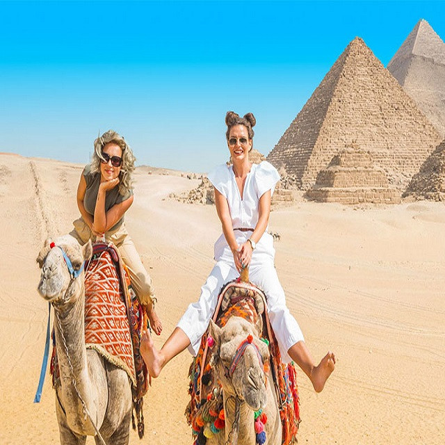 Travellers riding a camel in front of the Pyramids of Giza, Cairo, Egypt