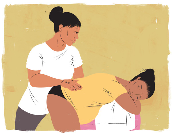 Doula pressing mothers back while she leans on birthing ball