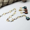 Atomic Knitting row counter chain featuring gold rings, white acrylic number beads (1-9), and squared czech beads with colourful patterns. Accented with metallic beads, the chain is displayed on a white background.