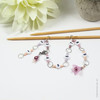 Pink and purple beaded chain row counter set for knitting, featuring white numbered beads from 1 to 9, silver rings, and a pink flower charm, displayed on bamboo knitting needles on a white background.