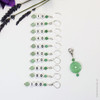 Set of ten green aventurine number stitch markers with silver rings, numbered 10 to 100, displayed with a green pressed glass progress marker, used for knitting and crochet projects.