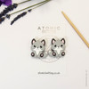 A pair of woodland fox needle stoppers in grey, shaped like cute foxes, placed on the tips of knitting needles to protect points and prevent dropped stitches.