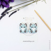 A pair of woodland fox needle stoppers in light blue, shaped like cute foxes, placed on the tips of knitting needles to protect points and prevent dropped stitches.