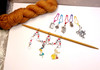 Overhead flat lay of complete Alice in Wonderland knitting set with row counter chain, five stitch markers and golden yarn hank on white background