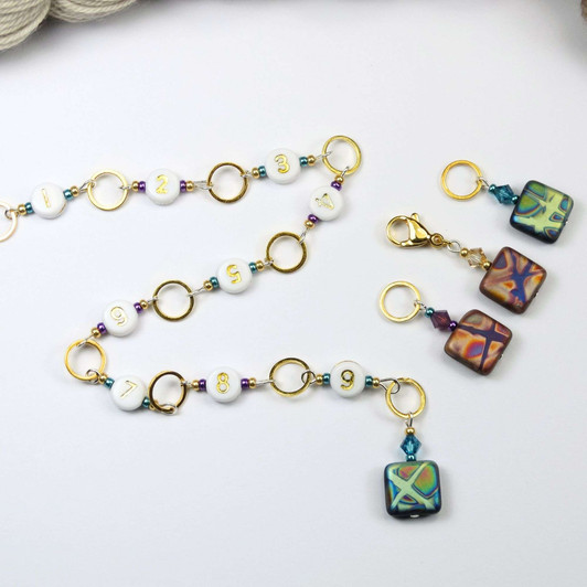 Atomic Knitting row counter chain featuring gold rings, white acrylic number beads (1-9), and czech beads with colourful patterns. Accented with sparkling beads, the chain is displayed on a white background.