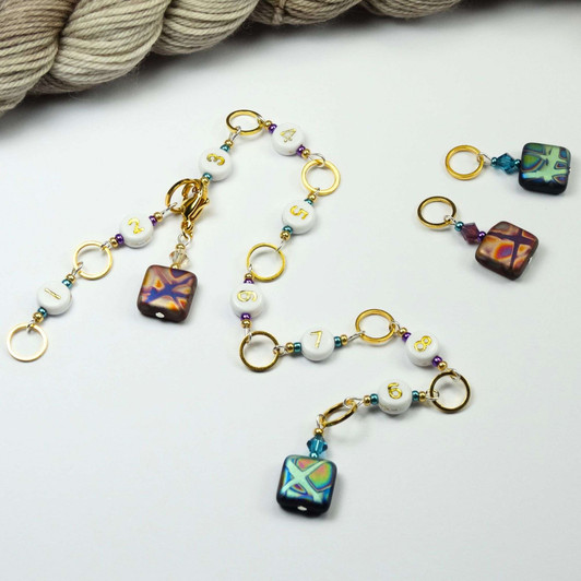 Atomic Knitting row counter chain featuring gold rings, white acrylic number beads (1-9), and czech beads with colourful patterns. Accented with sparkling beads, the chain is displayed on a white background.