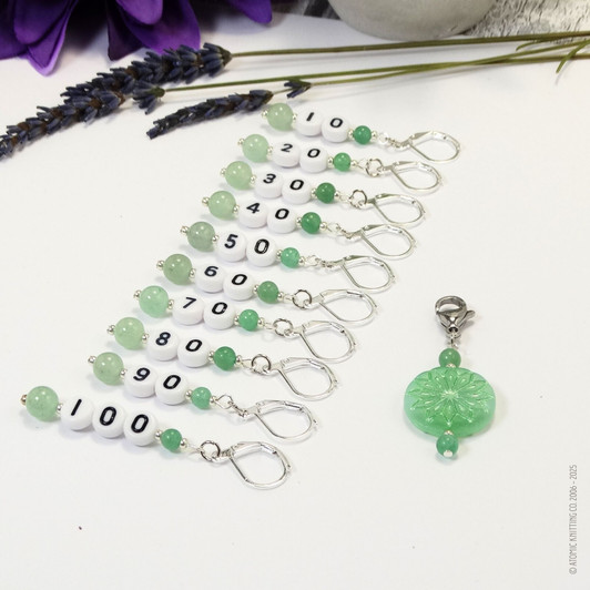 Set of ten green aventurine number stitch markers with silver rings, numbered 10 to 100, displayed with a green pressed glass progress marker, used for knitting and crochet projects.