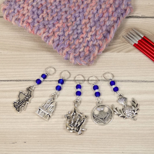 Set of 5 Stitch Markers with Scottish Themed charms and cobalt blue beads. Includes stitch markers with bagpipe, thistle, Scotland, castle and thistle charms.