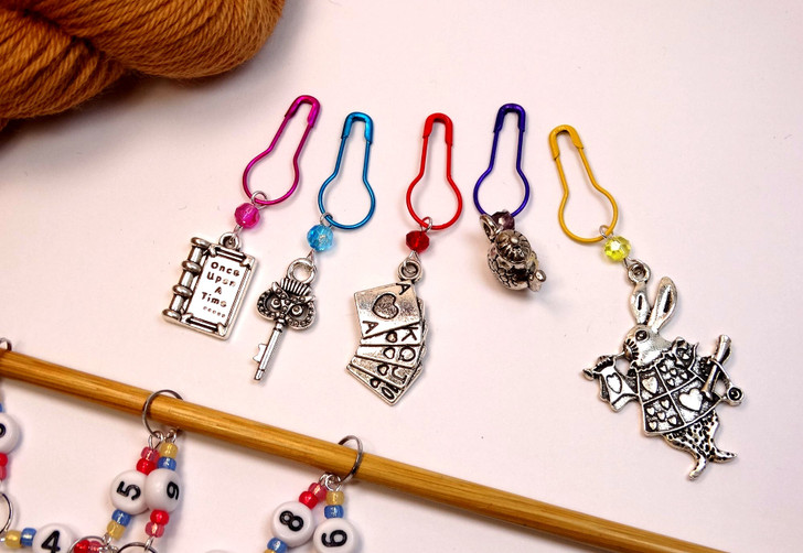 Close-up of Alice in Wonderland beaded row counter chain on bamboo knitting needle, highlighting numbered beads 1–9 with colourful seed beads and enamel Alice and White Rabbit charms