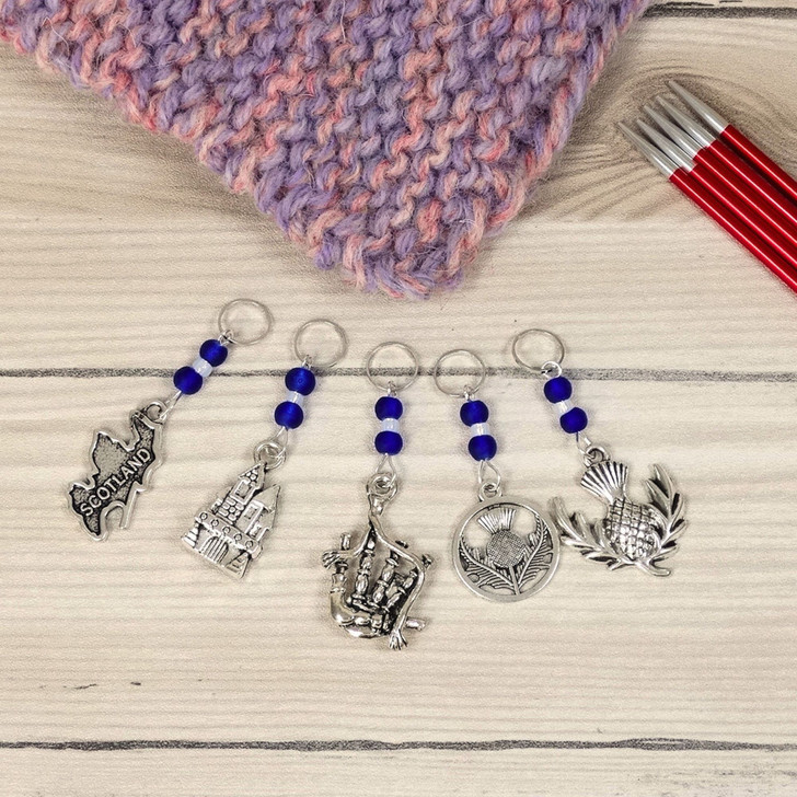 Set of 5 Stitch Markers with Scottish Themed charms and cobalt blue beads. Includes stitch markers with bagpipe, thistle, Scotland, castle and thistle charms.
