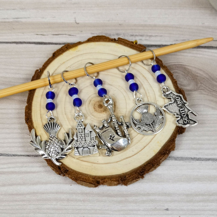 Set of 5 Stitch Markers with Scottish Themed charms and cobalt blue beads. Includes stitch markers with bagpipe, thistle, Scotland, castle and thistle charms.