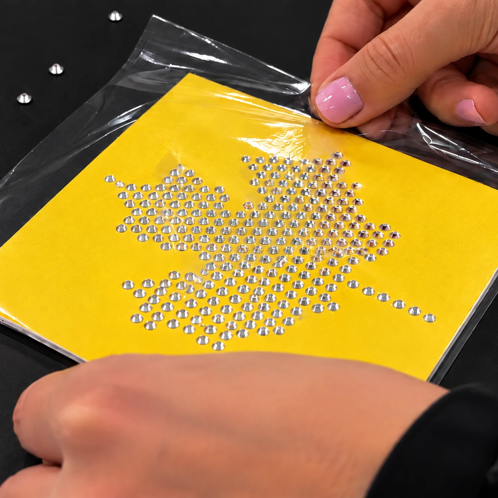 Applying clear rhinestone transfer tape over a completed maple leaf rhinestone design