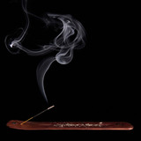 Smoking incense stick on a wooden holder, black background — scent inspiration for Patchouli fragrance oil