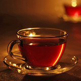 Glass cup of amber tea on a saucer, candlelit — scent inspiration for Pomegranate Cider fragrance oil