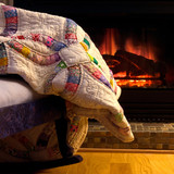 Patchwork quilt draped on a chair before a fireplace — scent inspiration for Fireside fragrance oil