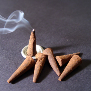 Brown incense cones with rising smoke on a dark surface — scent inspiration for Sandalwood fragrance oil