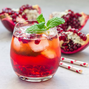 Red drink with mint and pomegranate seeds, split fruit behind — scent inspiration for Pomegranate Lemonade fragrance oil