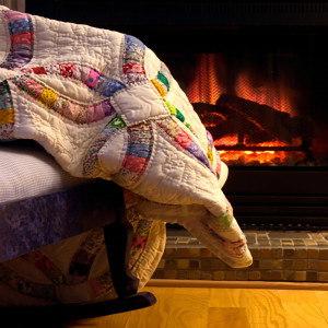 Patchwork quilt draped on a chair before a fireplace — scent inspiration for Fireside fragrance oil