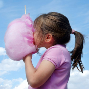 Girl eating pink cotton candy against blue sky — scent inspiration for Cotton Candy fragrance oil