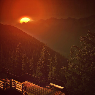 Orange sunset over forested mountains with a cabin roof — scent inspiration for Mahogany Woods fragrance oil
