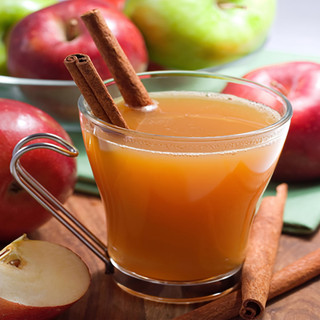 Glass mug of cider with a cinnamon stick and apples — scent inspiration for Mulled Cider fragrance oil