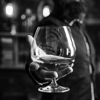 A hand holding a brandy snifter in a dim, blurred bar — scent inspiration for Bow Ties & Bourbon fragrance oil