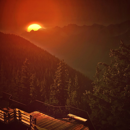 Orange sunset over forested mountains with a cabin roof — scent inspiration for Mahogany Woods fragrance oil