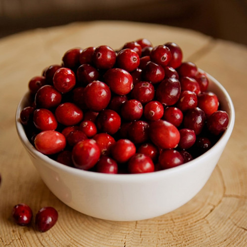 Red cranberries piled in a white bowl on wood — scent inspiration for Cranberry fragrance oil