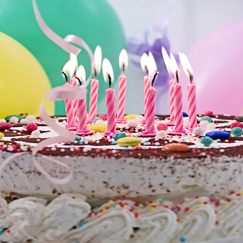 Lit pink candles on sprinkle cake with balloons behind — scent inspiration for Birthday Cake fragrance oil