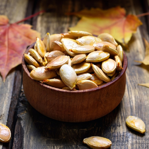 Wooden bowl of roasted pumpkin seeds with autumn leaves — scent inspiration for Pumpkin Seeds & Oud fragrance oil
