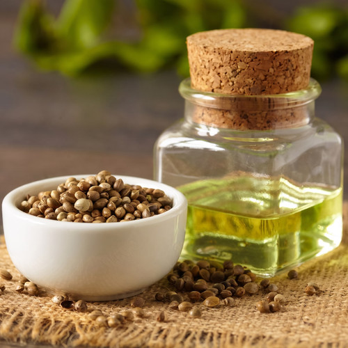 Hemp seeds in a white bowl beside a corked jar of green oil — scent inspiration for Cannabis & Exotic Hemp fragrance oil