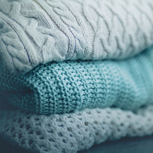 Stacked white and teal knit sweaters folded close-up — scent inspiration for Sweater Weather fragrance oil