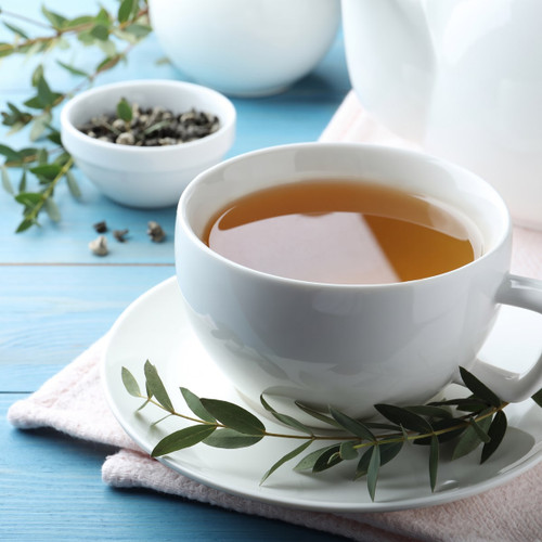 white cup of tea with green sprig on blue table — scent inspiration for Eucalyptus Tea fragrance oil
