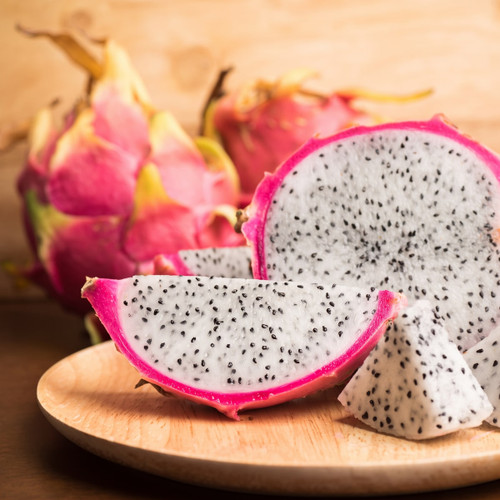 Halved dragon fruit with white black-seeded flesh on a wooden plate — scent inspiration for Dragon Fruit fragrance oil